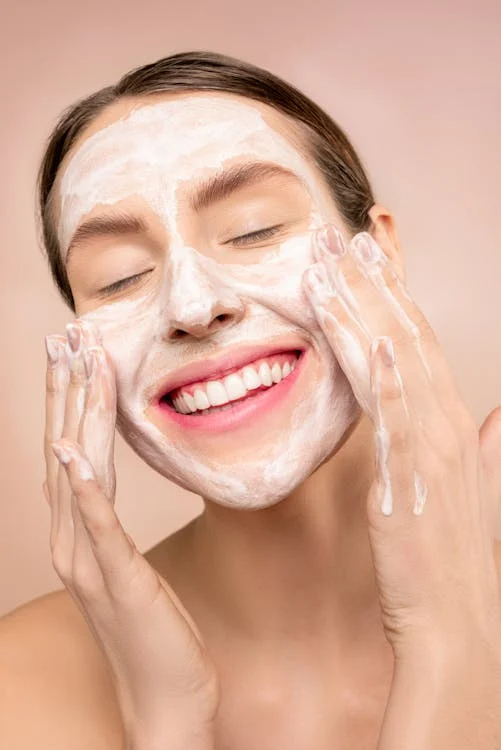 Close-up of a woman’s smiling face as she applies cream product on her face with hands.
